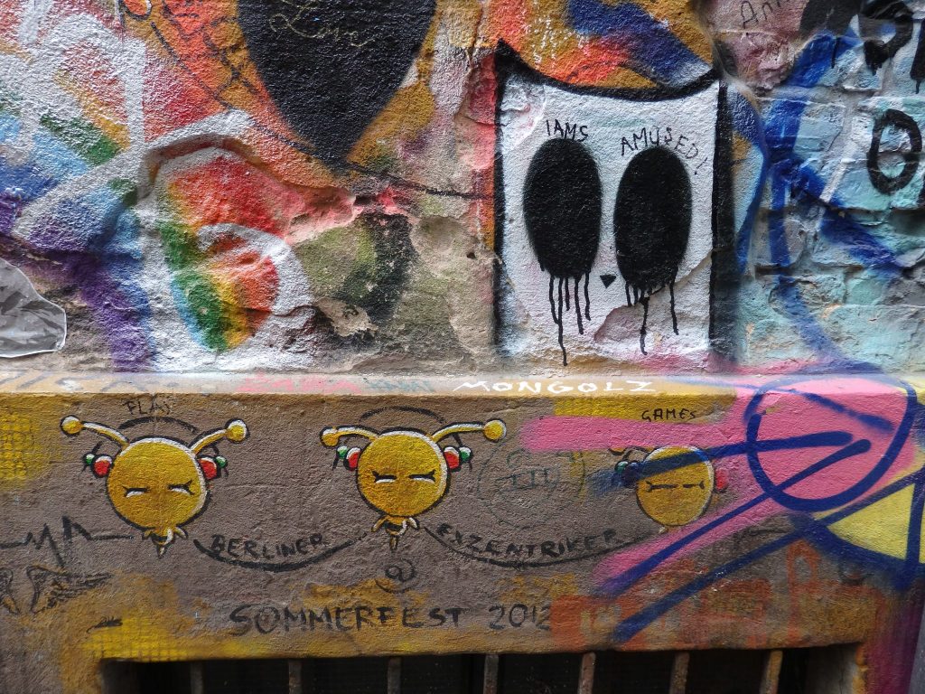 3 small yellow figures with antenna linked by the words "Berliner Exzentriker."