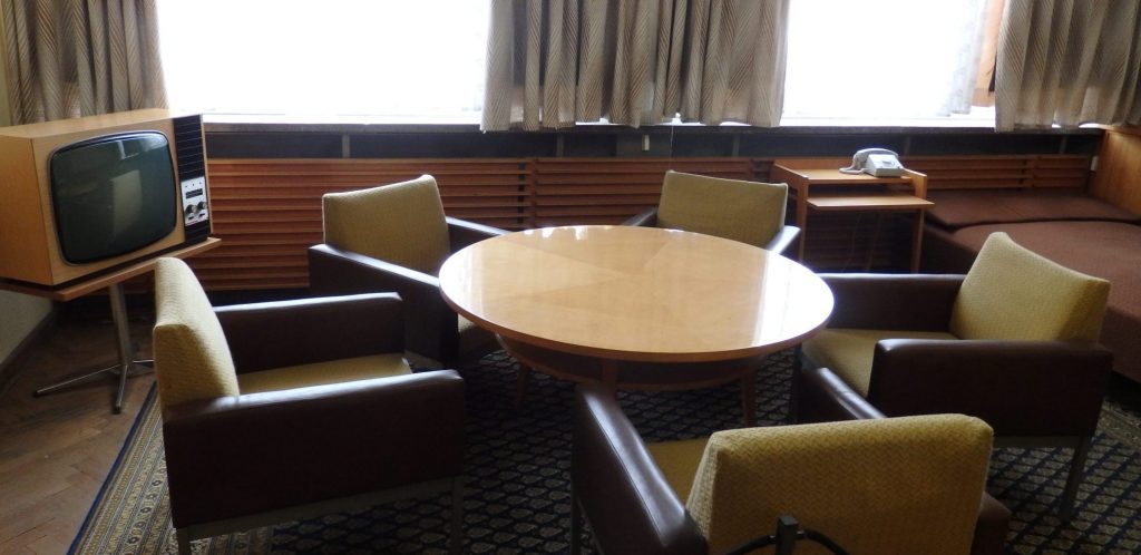 A  table with 5 armchairs around it in a very 60s style. Vintage TV in the corner.