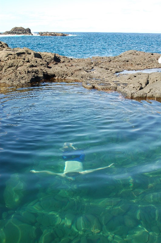 One person is visible, swimming toward the camera, under the water's surface. The water is clear and bluish-green and some rocks emerge from the water behind the swimmer.  Photo courtesy of Nat Harris