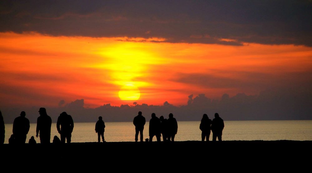 Sunset in Tuscany. In front, a row of people in sillouette. The sea beyond them with a spectacular orange and yellow sunset above the horizon. Photo courtesy of Sandy Swanton