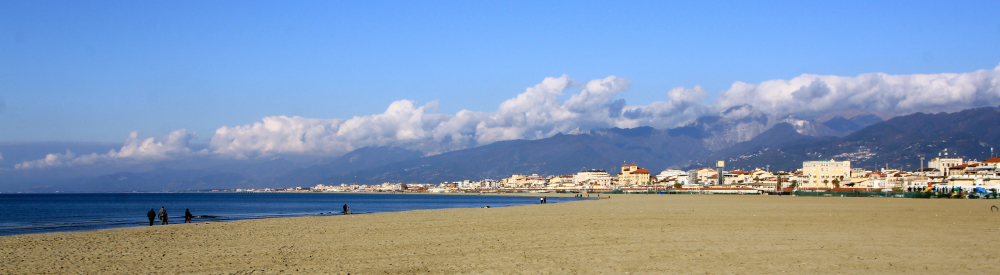 Looking north toward Cinque Terre. On the left, the sea. In front, a beach. In the distance, a low-rise cityscape backed by cloud-topped mountains. Photo courtesy of Sandy Swanton.