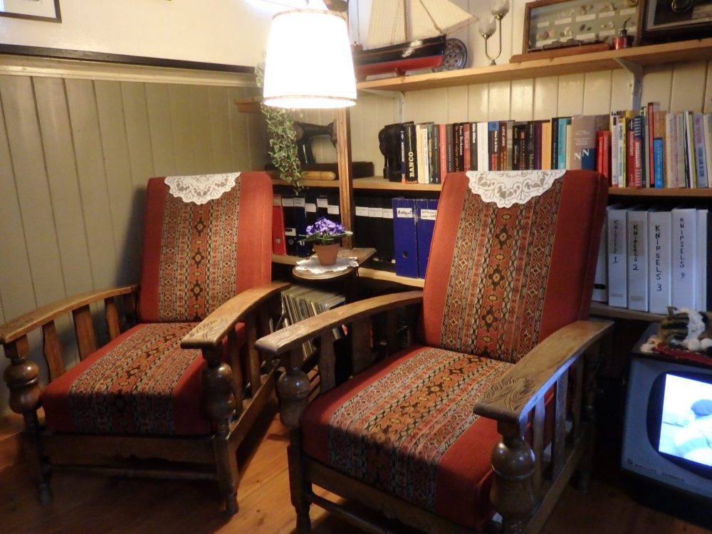 A comfortable corner of the living room in the Houseboat Museum: two armchairs in front of a bookshelf full of books.