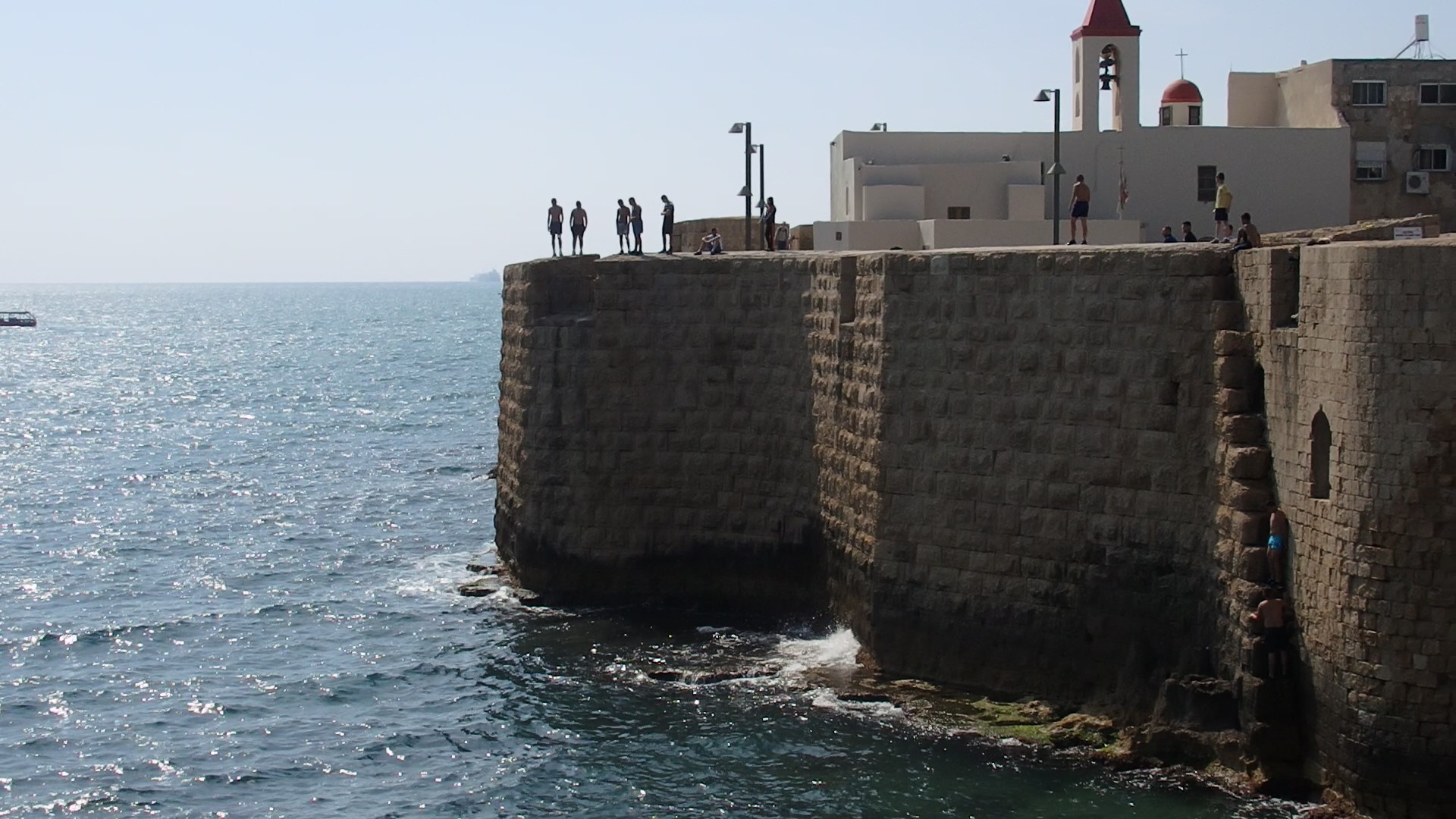 A view of the wall around Akko old city. Notice the boys preparing to jump from the wall, and, on the bottom right, a couple of boys climbing up from the water.