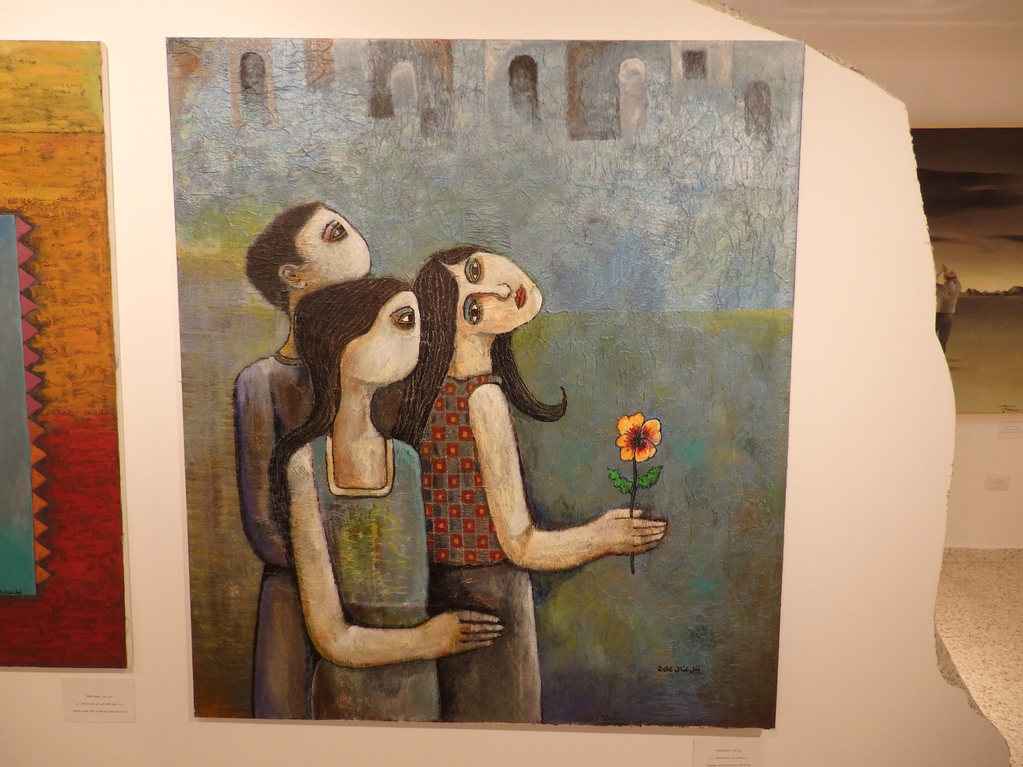 2 women and one man in a slightly picasso-esque style looking in different directions. One holds a yellow flower.