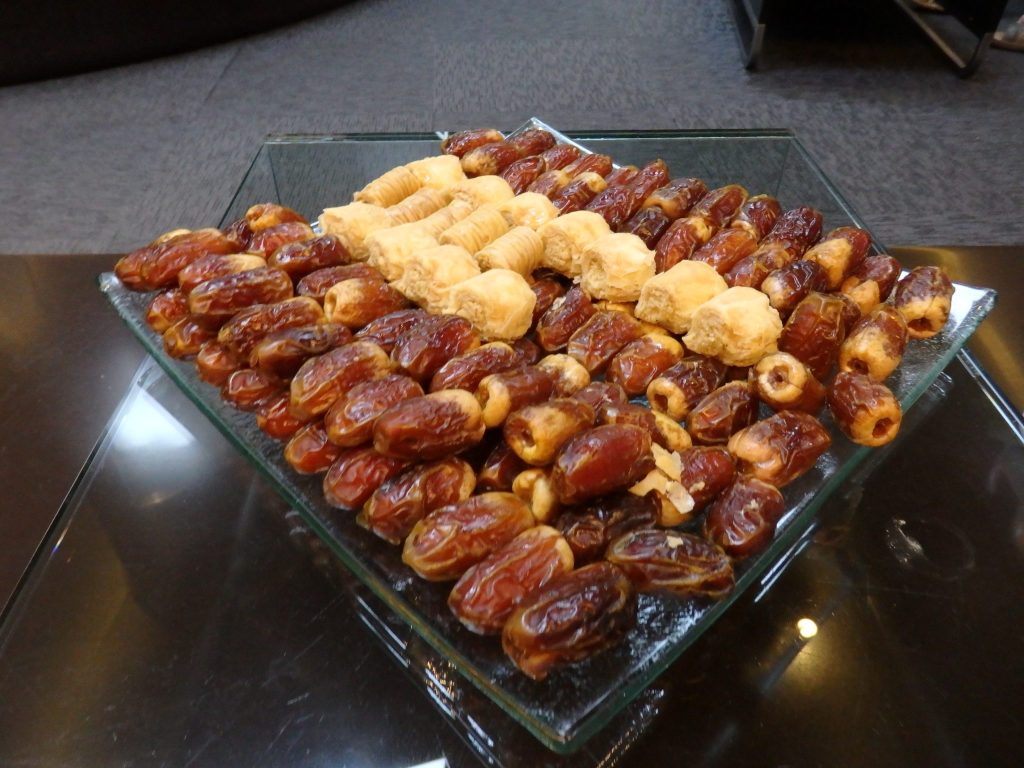 A rectangular try with small items in neat rows: mostly dates and small pastries.