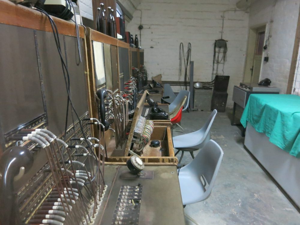 The long switchboard extends along the left-hand wall, with wires connecting the plugs to plugs. Chairs face the switchboard.