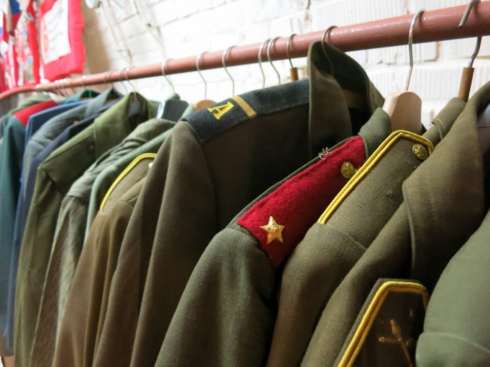 The coats hanging on the rack are almost all khaki green, and have insignia on the shoulders. One is red on the shoulder with yellow stars. Macabre sightseeing in Brno