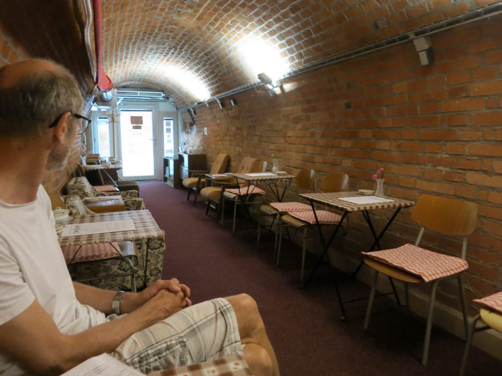 The tunnel here is fairly wide, enough for each side to have room for a row of small square tables and chairs. The walls are brick and so is the arched ceiling. IN the background, a glass door ends the tunnel. It's light outside the door. In the foreground is my husband, Albert, sitting in a chair against the wall, looking away from the camera toward the door. Macabre sightseeing in Brno