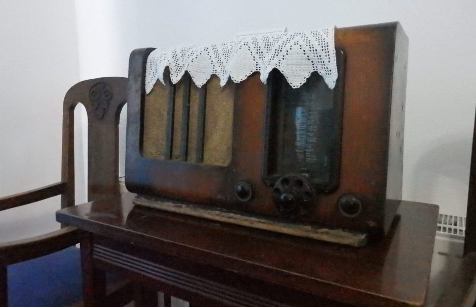 A wooden radio set on a wooden table, with a lace doily on top of it.
