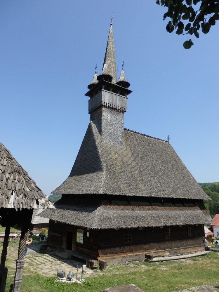 Budesti church: wooden with a shingle roof with two layers of eaves and a small tower with 4 little turrets around a central taller one. Wooden churches of Maramures