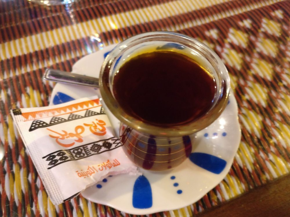 a very small glass with dark brown liquid and a packet of sugar.