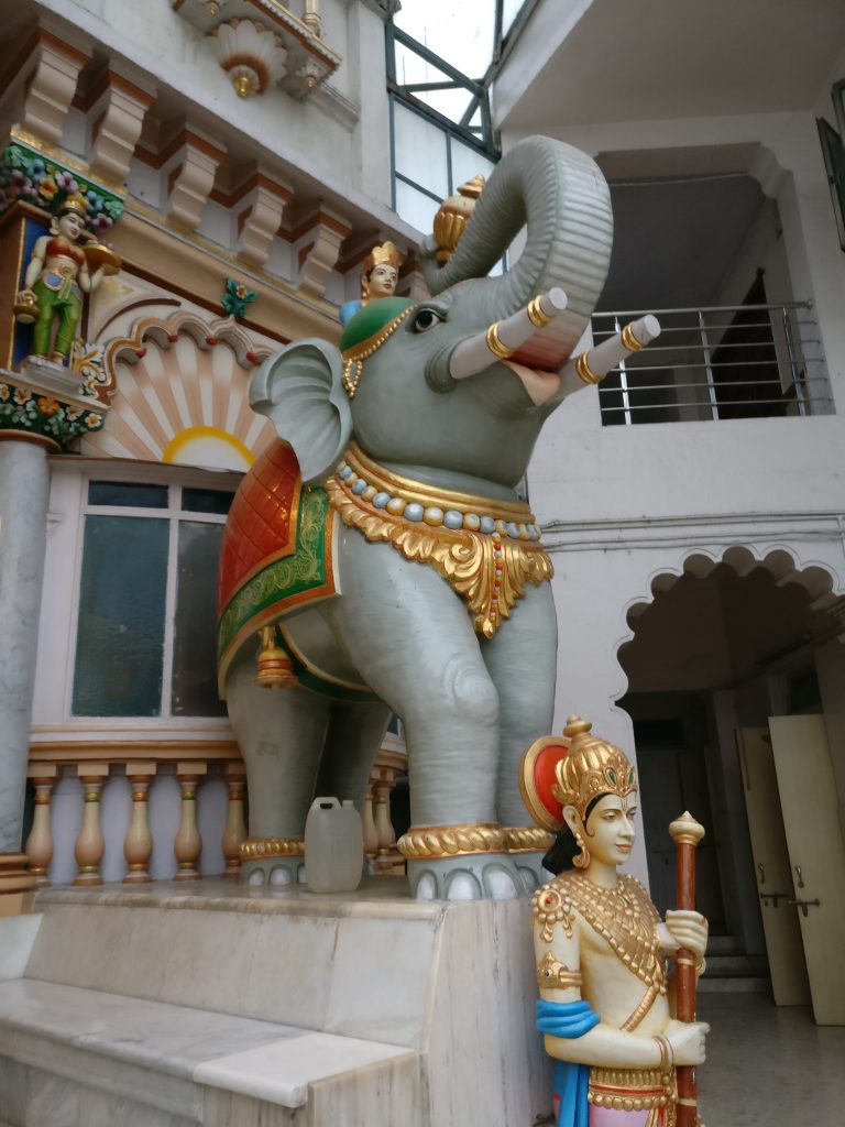 A statue of an elephant with trunk raised, and full-sized human statue in front of it.