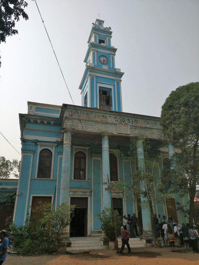 A blue-painted building with columns on the front and a tall spire in its center.