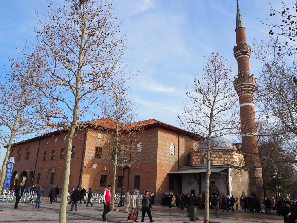 A large building on the left in stripes of light and red brick. Beside it, a very small building with a dome, and beside that, a tall narrow minaret.