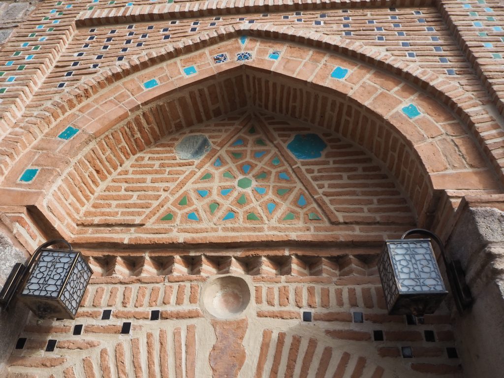 The door has a pointed arch above it, with insets of blue and green tile between the red bricks, forming a pretty pattern.