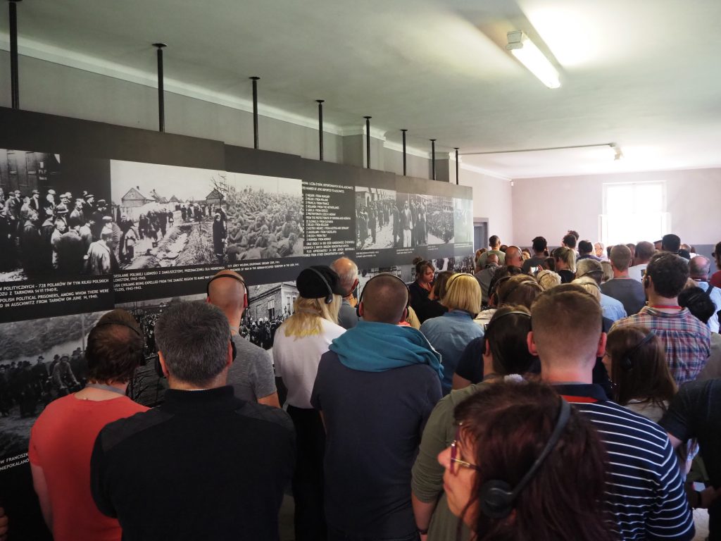 A wall of photos and text and lots of people in a wide area next to it.