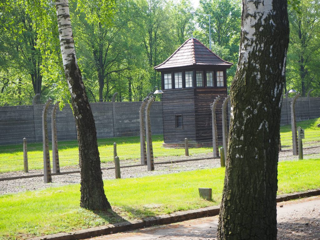 A view of one of the watchtowers next to a wall, with two rows of barbed-wire fences in front of it.