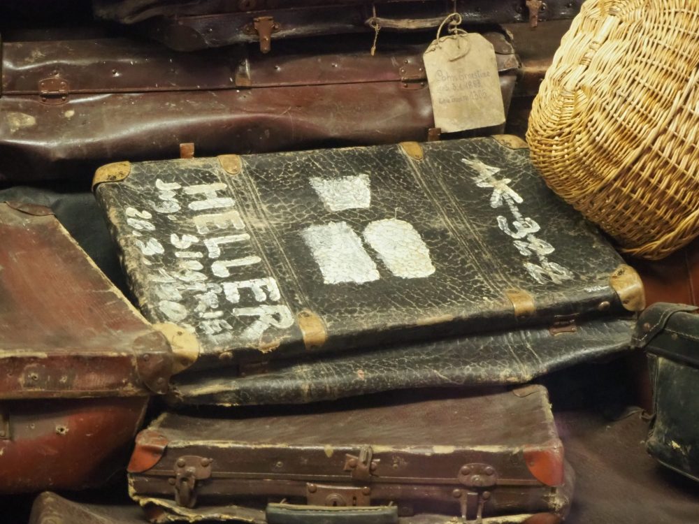 The suitcase is dark leather, well-used and dusty. The writing is in white paint. It is among many similar suitcases.