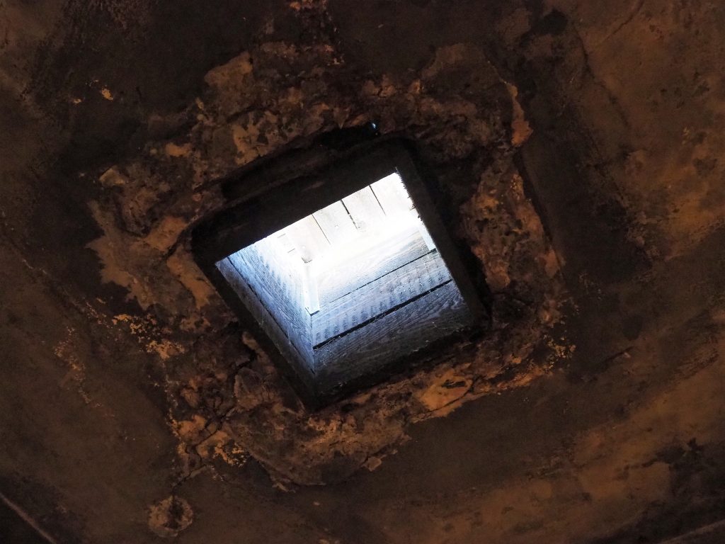 A rough cement ceiling with a square hole admitting light.