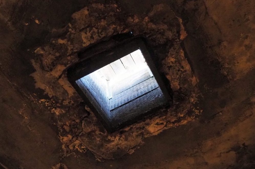 Dark, rough stone or cement ceiling and bright light through a small square hole.