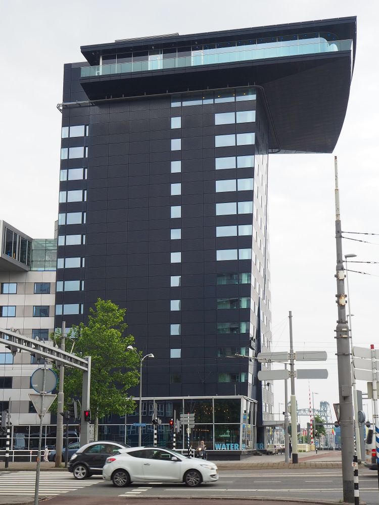 A tall dark building of perhaps 17 stories, but the top two stories stick way out from the rest of the building, like a giant porch with glass sides.