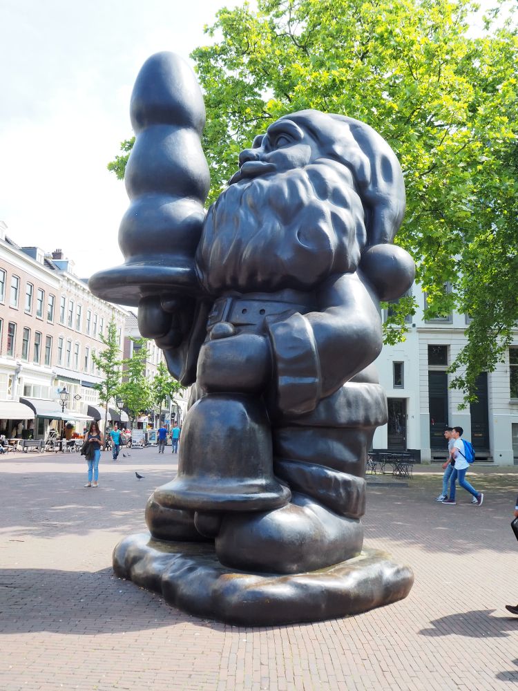 This large statue depicts a santa clause with beard and pompom hat. In one hand he holds a large bell. In the other, he's holding what is meant to be a Christmas tree. The problem is that the form of the tree is smoothed down and narrowed, so it looks like a butt plug. 