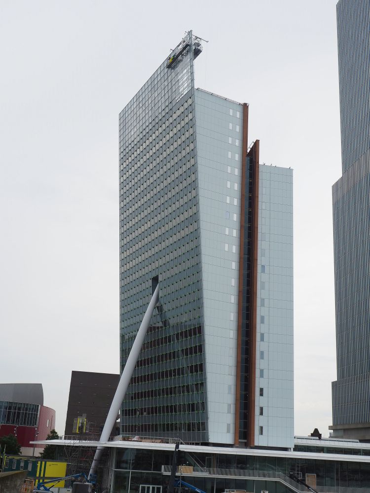 The building looks like a regular glass-sided skyscraper, except that one of the long sides leans out. A huge beam extends from the ground up to the middle of the leaning facade, where it seems to fit into a hole. It makes it look like it's holding up the building. 