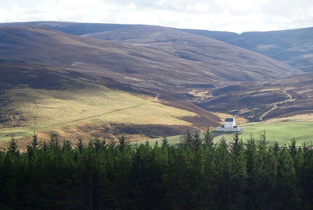 A valley between rather barren hills, with trees in the foreground and a small white castle in the valley.