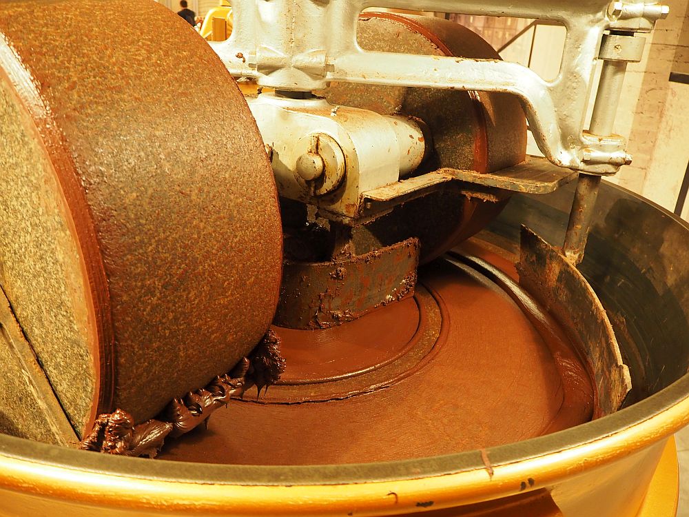 The machine has large stone or concrete wheels that roll in a circle, crushing the chocolate as they turn.