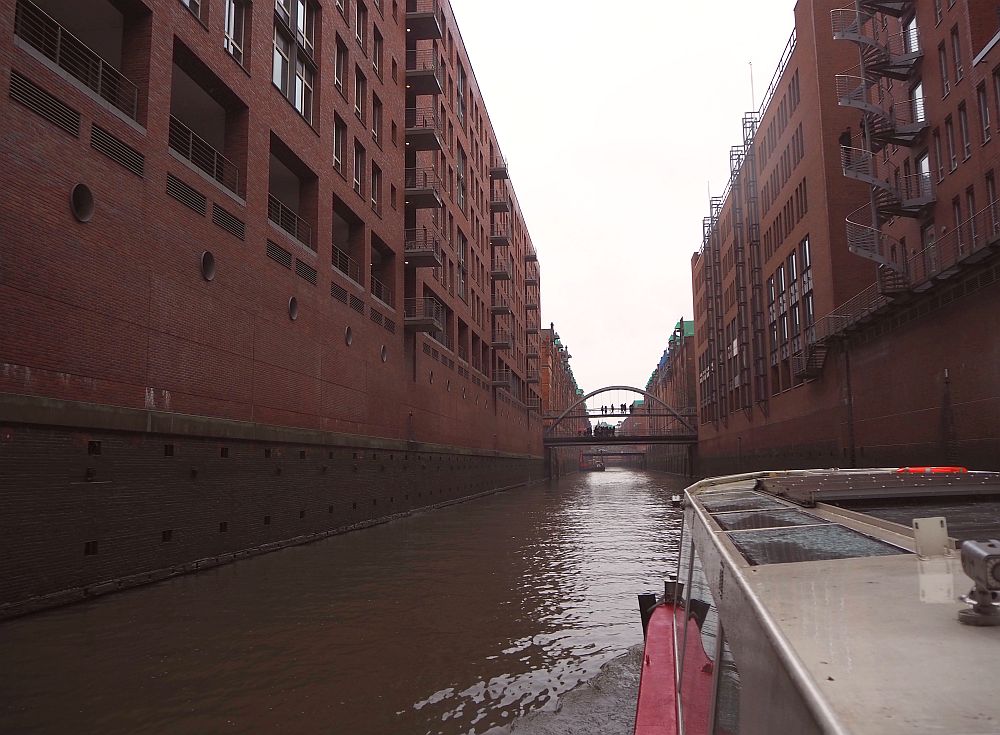 red-brick warehouse buildings line the canal, and a small arched pedestrian bridge is visible ahead. Hamburg for a weekend.