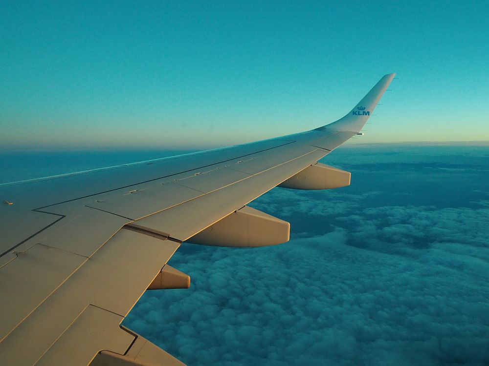 a view of an airplane wing over fluffy clouds, with a sunset sky in the background