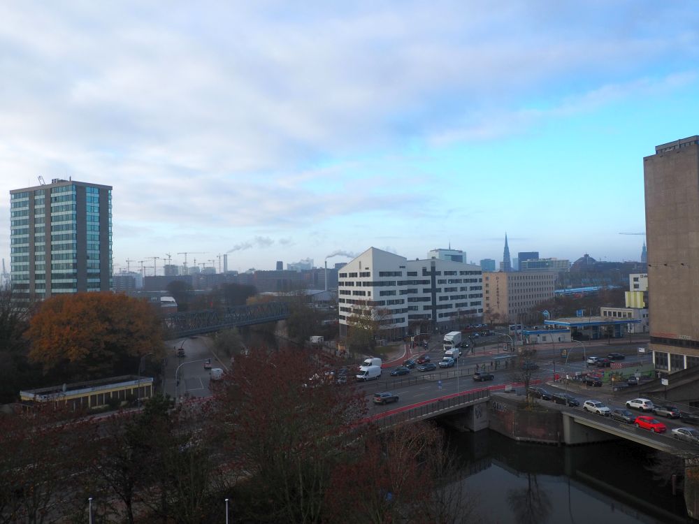 Mixed urban view: some taller buildings, some smokestacks, a church spire in the distance.