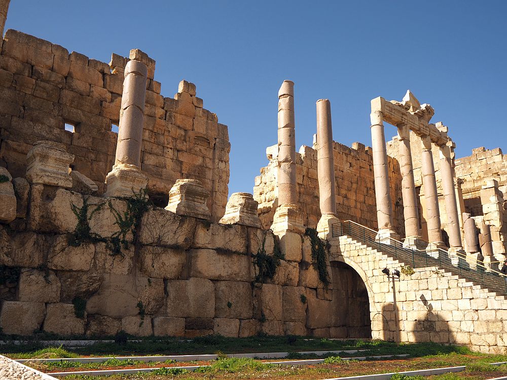 the entrance to the Baalbek ruins, and in particular the Temple of Jupiter has a few remaining pink granite columns in a row, at the top of a stone stairway. The bases of more pillars along the edge of the building remain. Behind that is a wall made of large stones that would have formed the back wall of the pillar-lined portico.