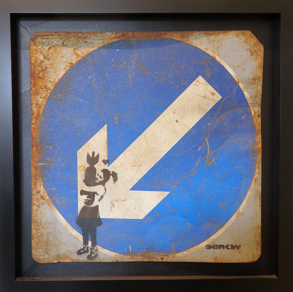 On a traffic sign of a white arrow on a blue background, the stencil shows a young girl hugging a rocket.