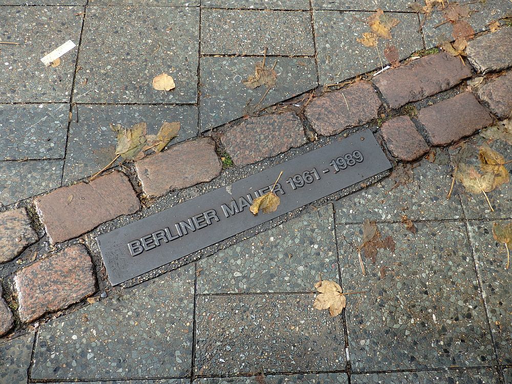 Red bricks in two lines cut diagonally through the sidewalk pavings stones.