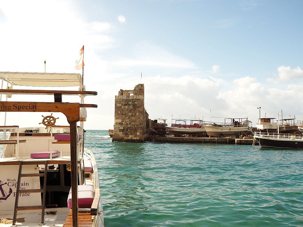 A partial view of the little Byblos harbour, with an ancient tower guarding the entrance. A moored tourist boat in the foreground. 
Special places in Lebanon: Byblos harbour.