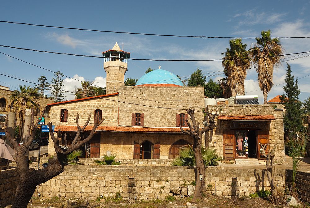 The mosque is made of stone blocks and has a stone minaret and a blue dome.