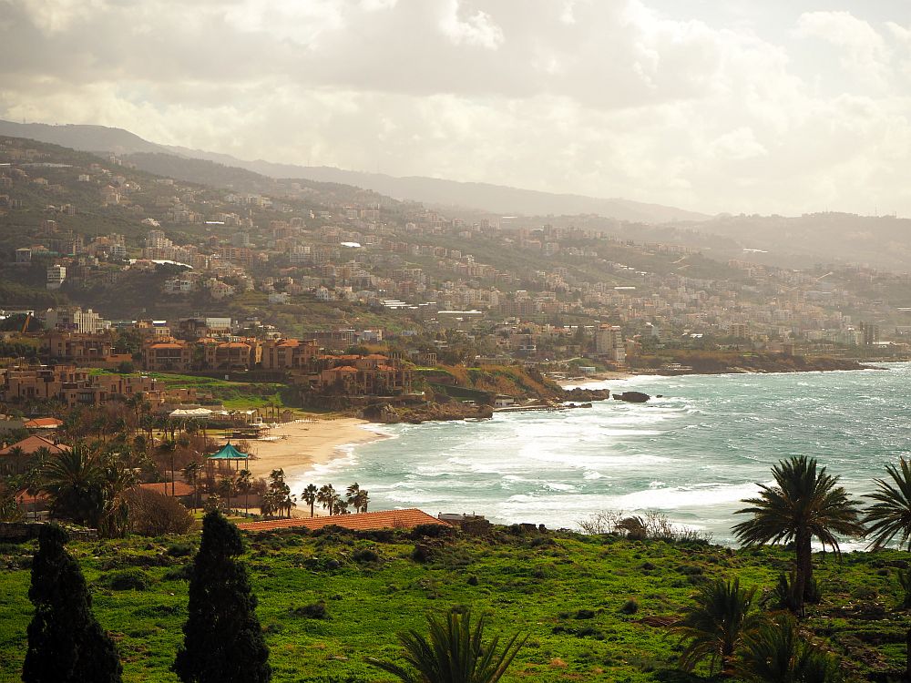 Buildings cover the hills rising from the coast. Waves hitting a beach are visible in a cove.