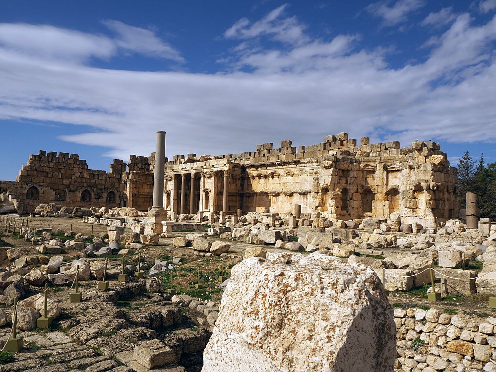 Nearby the ground is scattered with random pieces of rubble. In the background is an altar with pillars and a few extra rows of darker stone on top. At Baalbek ruins in Lebanon.