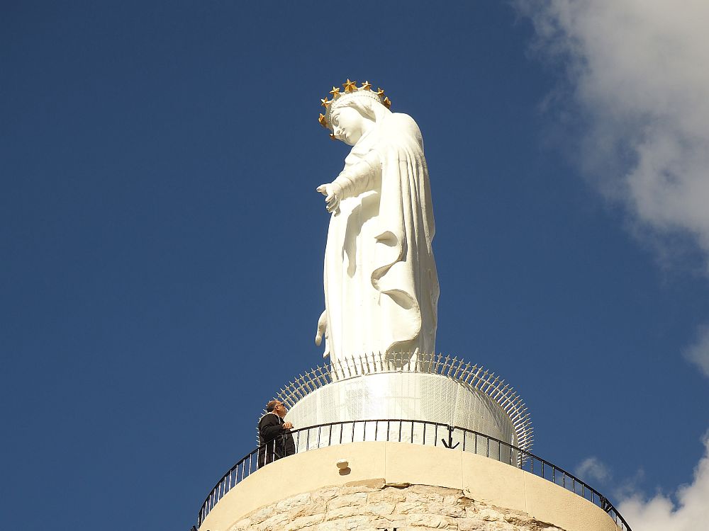 A large white figure of a woman in flowing robes and a golden crown. She has her hands outstretched at her side, palms facing outwards. 
Special places in Lebanon: Harissa.