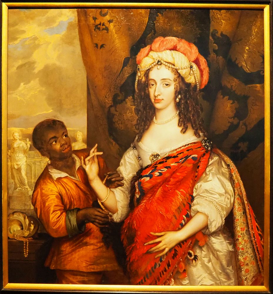 The woman's dress is white, but mostly hidden by the red feathered cloak. The servant boy stands slightly behind her, looking up at her, and helping her put on a bead bracelet.