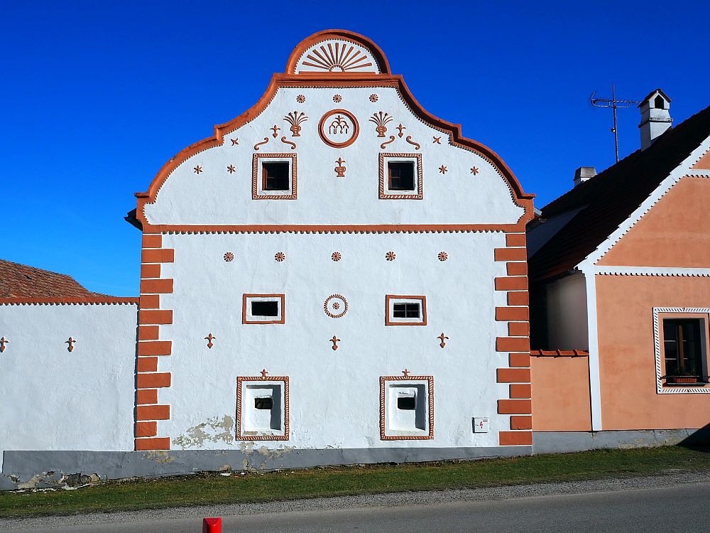 A simple square house with a peaked roof: white paint with pinkish accents.