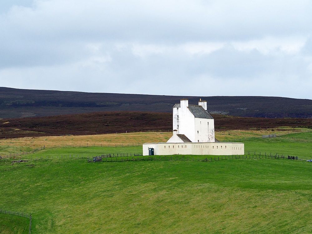 the building is vertical and simple and painted white, with a low, whitewashed wall around it, in the middle of a field.