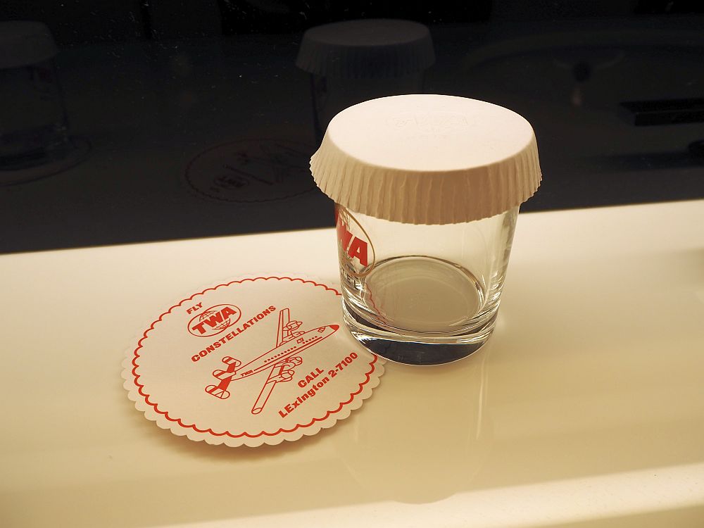 In the bathroom, a glass with the TWA logo and a coaster that reads "Fly TWA Constellations. Call LExington 2-7100.