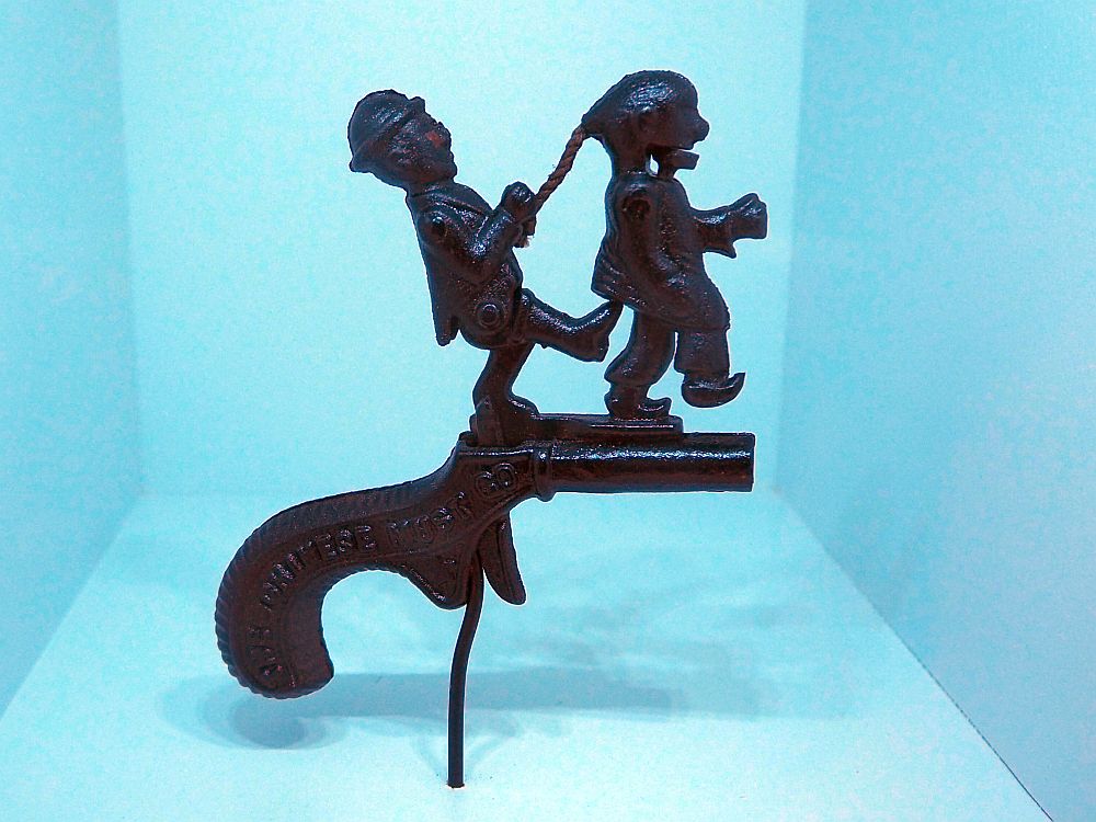 On top of the pistol's barrel, a man holds a Chinese man by the ponytail and kicks him.