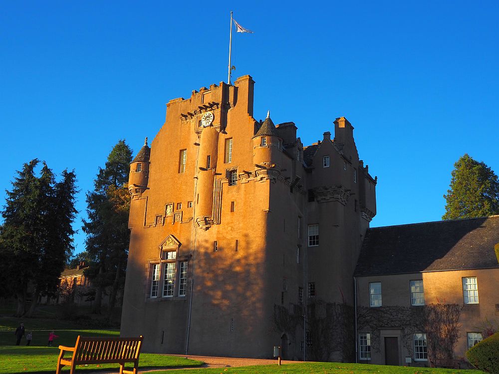 The whole building is visible with its little towers and crenellations. It is tinted orange in the sunlight against a blue sky.