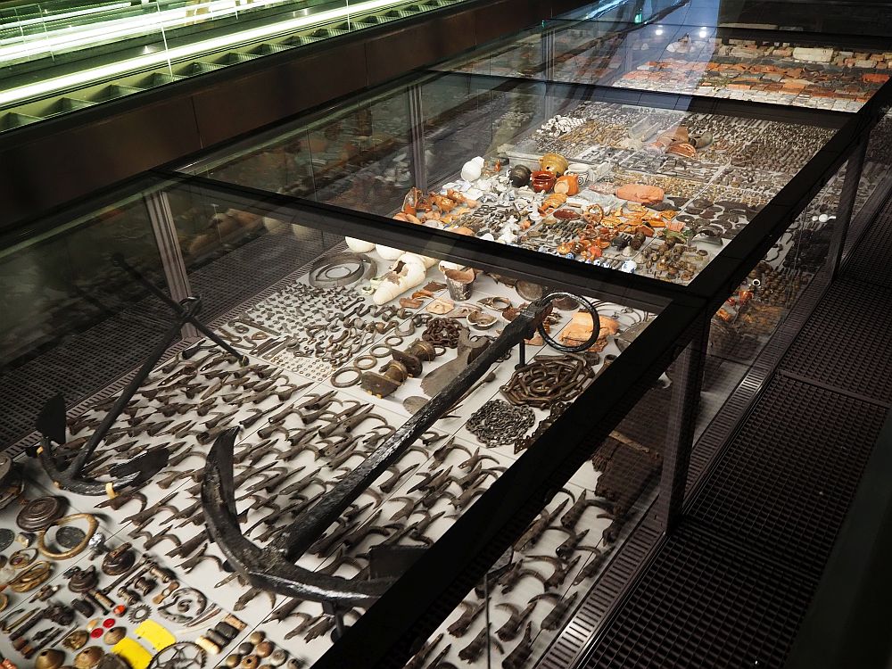 A glass-enclosed display case, with inbuilt lights illuminating the objects inside, closely packed together.