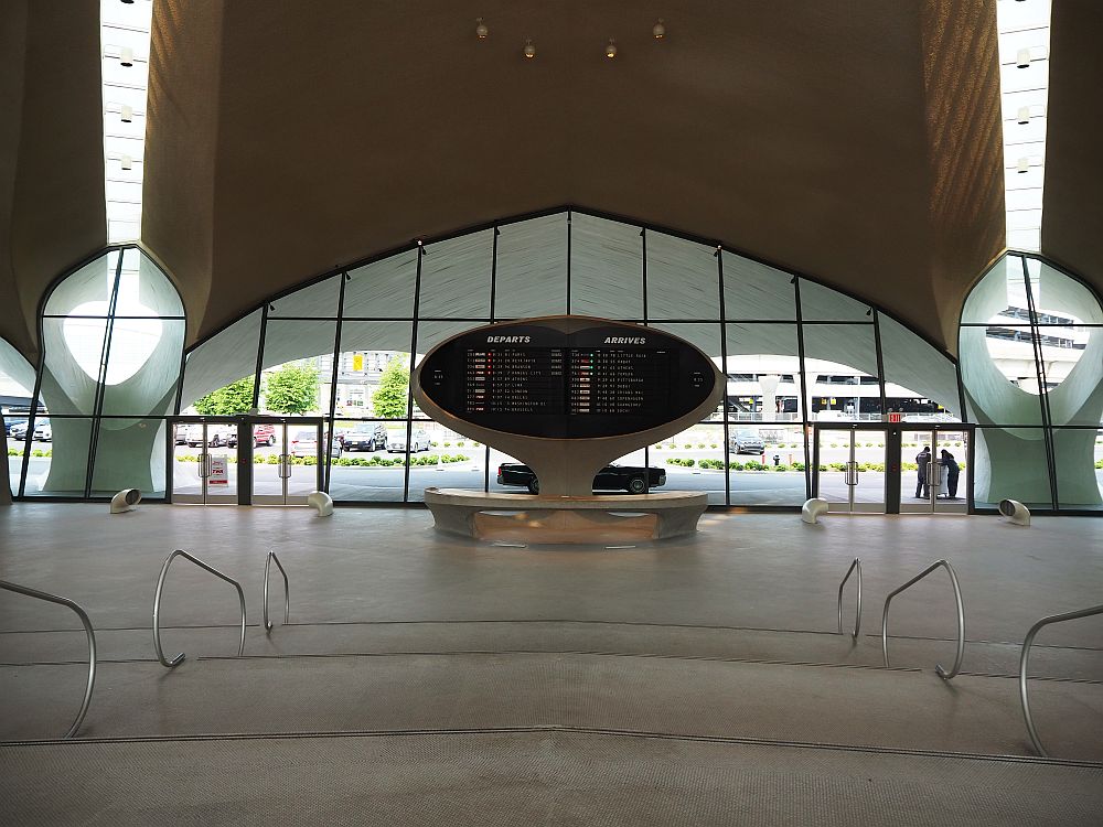 A large curved arch encompasses the entrance, with curved ceiling above it. In the center is an old-fashioned split-flap departures board.