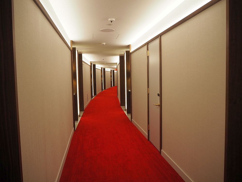 The hall is white-walled and red-carpeted and curves gently to the right.