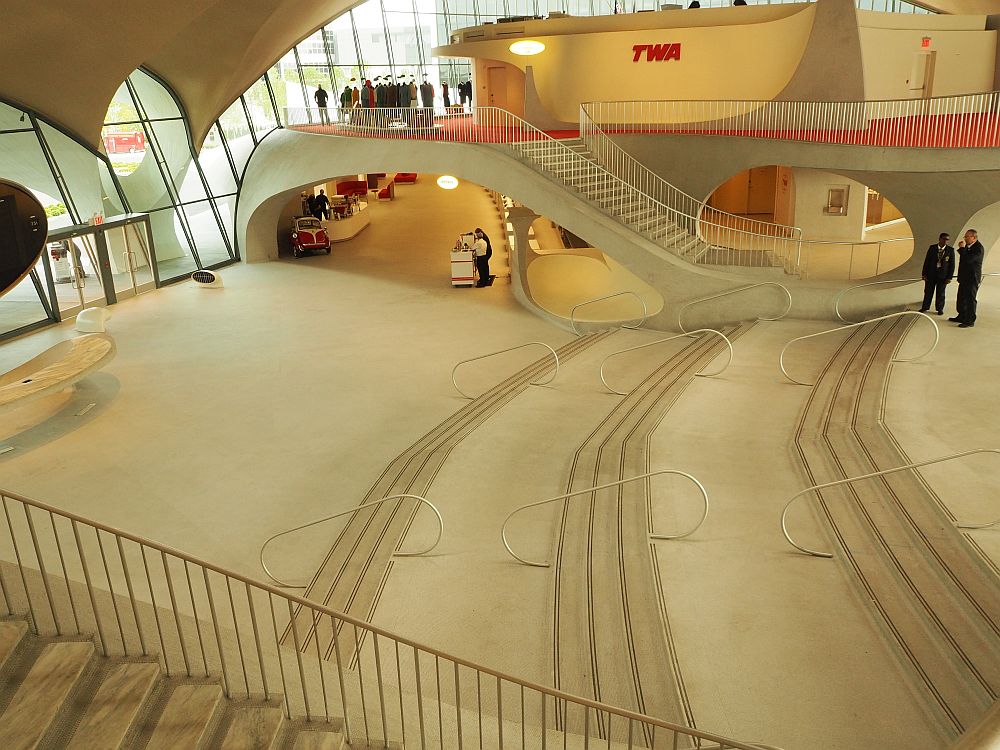 The lobby is very wide and white floored and empty, with shallow stairs leading up from left (the entrance) to the right side of the picture.